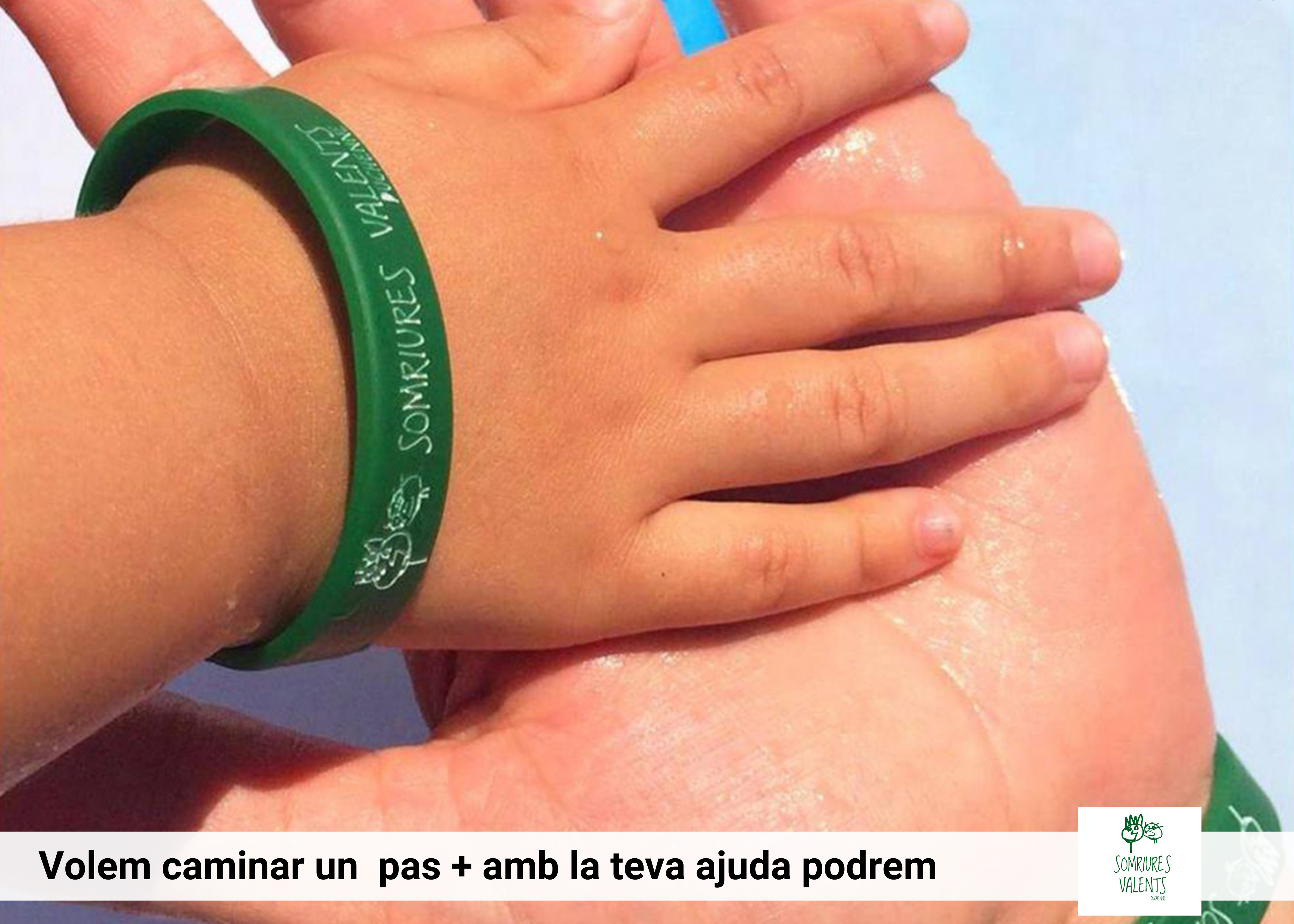  25.- Peu de foto, logo de l’Associació Somriures Valents. Fotografia d’una mà infantil que toca una mà d’un adult amb polseres de l'associació.