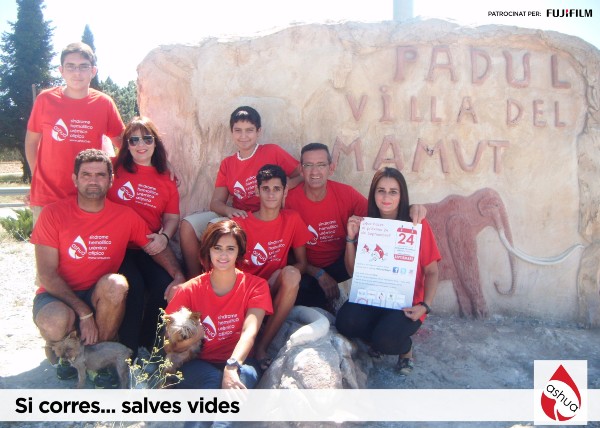 Peu de foto, logo de l’Associació Síndrome Hemolític Urèmic Atípic ( ASHUA). Fotografia  d’un grup de  famílies amb les samarretes amb el logo de l'associació en un paisatge de roques.