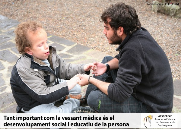  15.- Peu de foto, logo de l’Associació Catalana Pro Persones Sordcegues (APSOCECAT). Fotografia d’un nen i un jove assentats sobre un terra de pedra, cara a cara agafant-se les mans. 