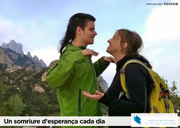 Peu de foto logo de l'Associació Nacional d’Esclerosi Tuberosa, fotografia d’un jove i una mare amb actitud carinyosa amb les muntanyes de Montserrat al fons